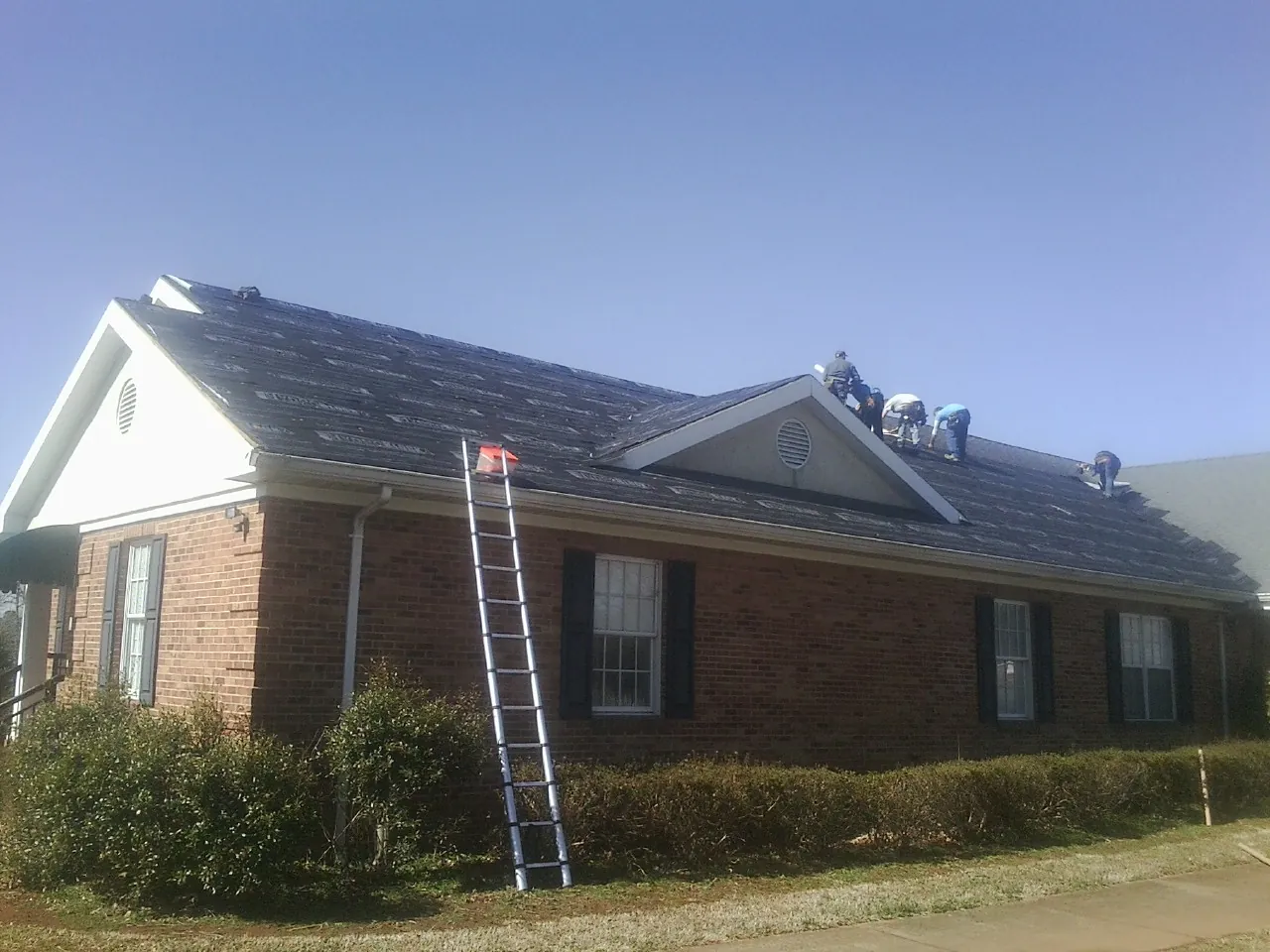 Crew tearing shingles off a brick ranch roof with a ladder set — Metal Roof Repair work by our crew in Bloomsbury