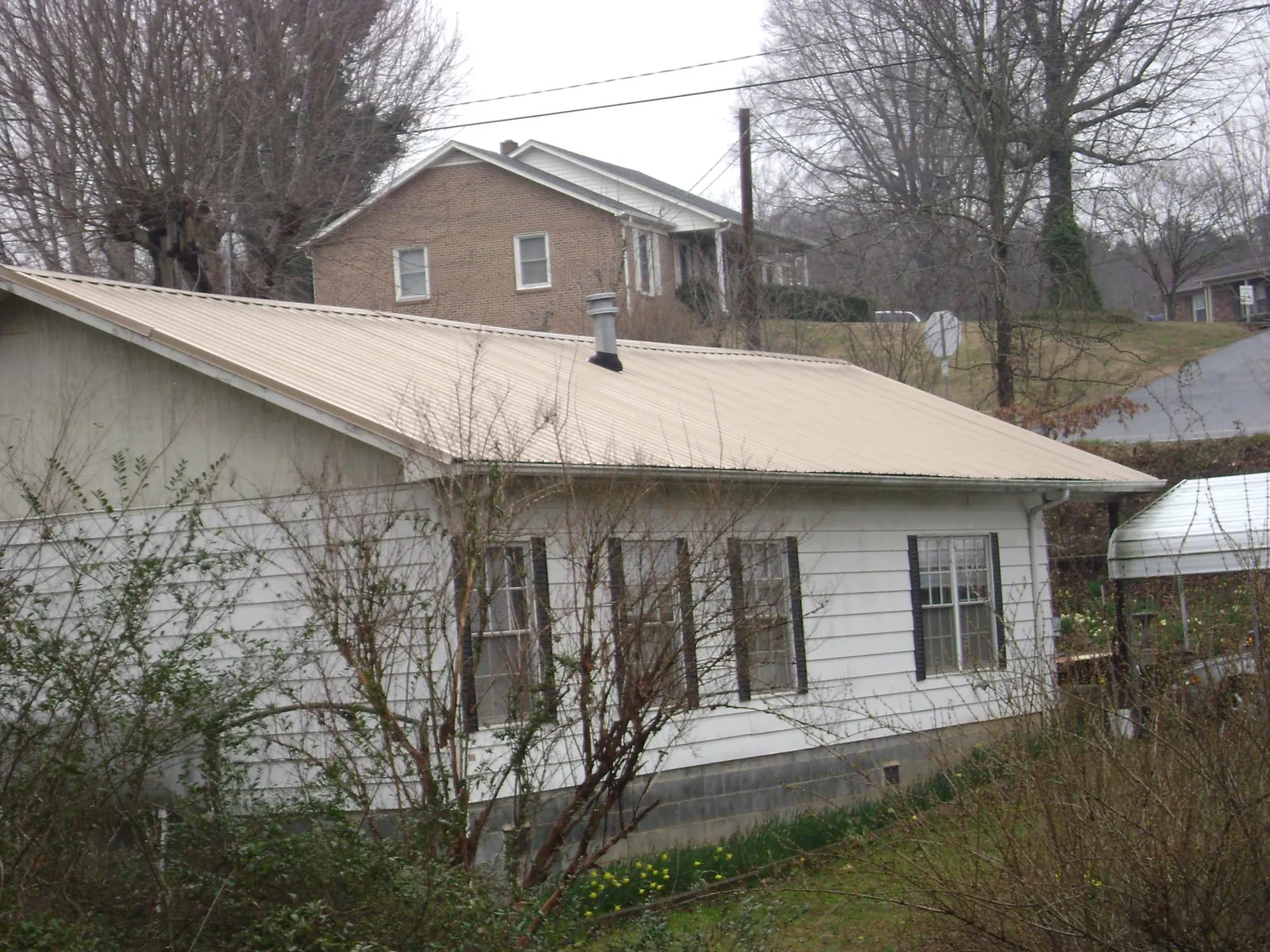 Tan metal roof on a white sided house set into a hillside — Commercial Roofing by Roofing Brothers in Bloomsbury